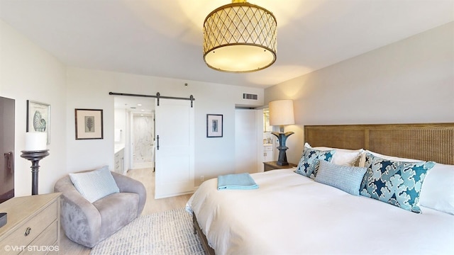 bedroom with a barn door, connected bathroom, and light hardwood / wood-style floors