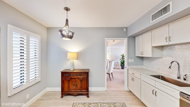 kitchen featuring sink, white cabinetry, light wood-type flooring, pendant lighting, and decorative backsplash