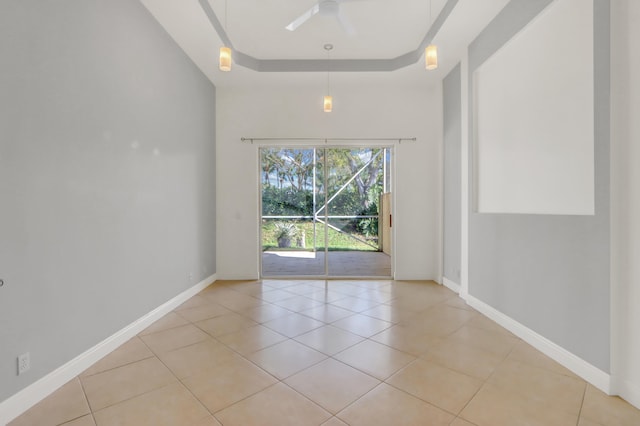 empty room with ceiling fan, light tile patterned floors, and a tray ceiling