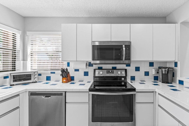 kitchen with stainless steel appliances, white cabinetry, a textured ceiling, and backsplash