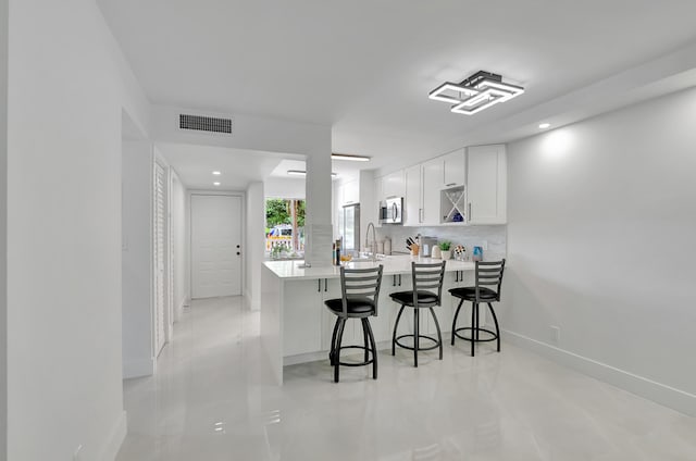 kitchen featuring white cabinets, sink, kitchen peninsula, a breakfast bar area, and backsplash