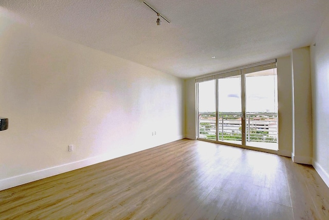 empty room with a wall of windows, light wood-type flooring, track lighting, and a textured ceiling