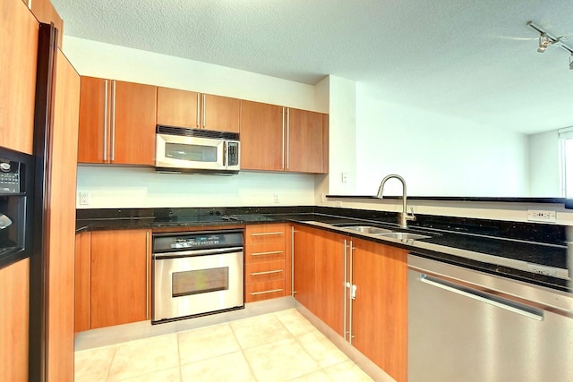 kitchen featuring a textured ceiling, track lighting, sink, stainless steel appliances, and dark stone countertops