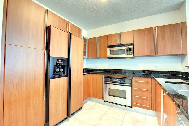 kitchen with appliances with stainless steel finishes, a textured ceiling, dark stone countertops, and sink