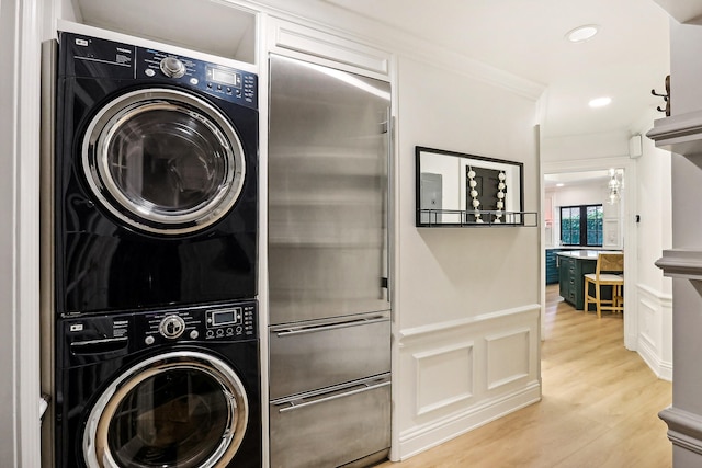 clothes washing area with stacked washer and dryer, crown molding, and light hardwood / wood-style floors