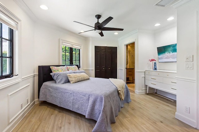 bedroom with light wood-type flooring, ceiling fan, crown molding, connected bathroom, and a closet