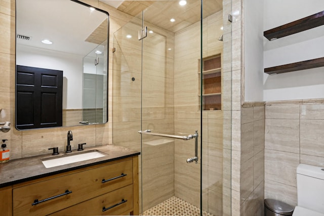 bathroom featuring vanity, toilet, a shower with door, and tile walls