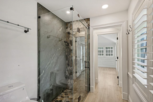 bathroom with hardwood / wood-style floors, toilet, and a shower with door