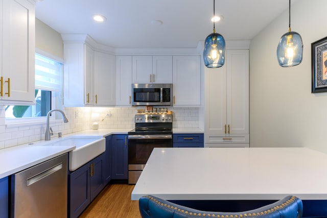 kitchen with appliances with stainless steel finishes, white cabinets, backsplash, decorative light fixtures, and hardwood / wood-style floors