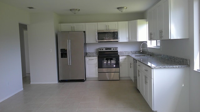 kitchen featuring light stone countertops, sink, light tile patterned flooring, white cabinetry, and appliances with stainless steel finishes