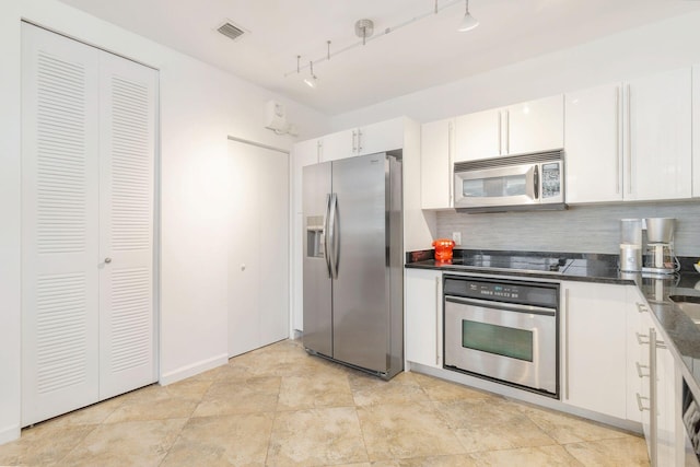 kitchen with dark stone countertops, white cabinetry, backsplash, stainless steel appliances, and track lighting