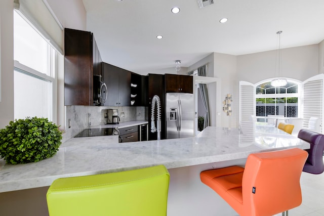 kitchen with kitchen peninsula, pendant lighting, stainless steel appliances, dark brown cabinetry, and a chandelier