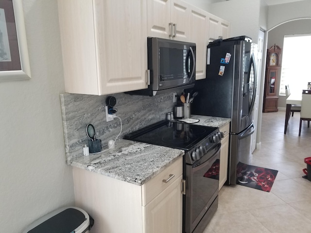 kitchen with appliances with stainless steel finishes, light stone countertops, light tile patterned floors, and backsplash