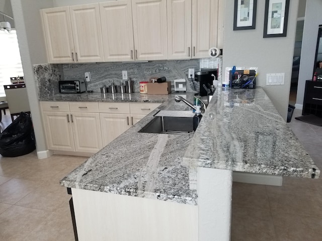 kitchen with light tile patterned floors, light stone countertops, sink, and decorative backsplash