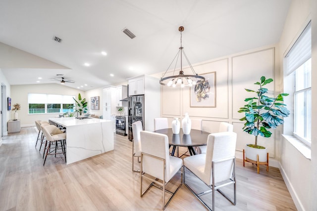 dining space with light hardwood / wood-style floors, sink, ceiling fan with notable chandelier, and vaulted ceiling