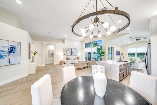 dining area featuring ceiling fan with notable chandelier, sink, lofted ceiling, and light hardwood / wood-style flooring