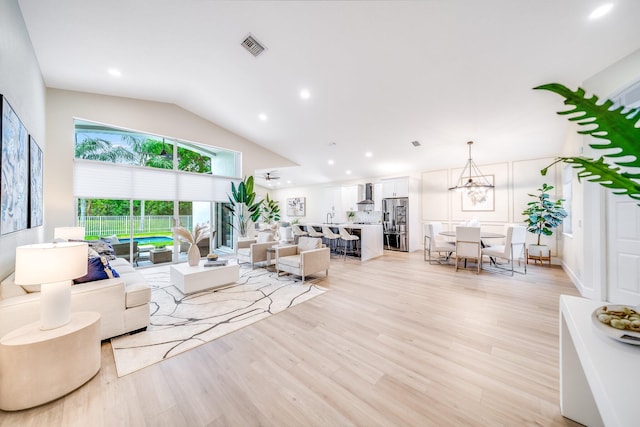 living room featuring vaulted ceiling, an inviting chandelier, and light hardwood / wood-style floors