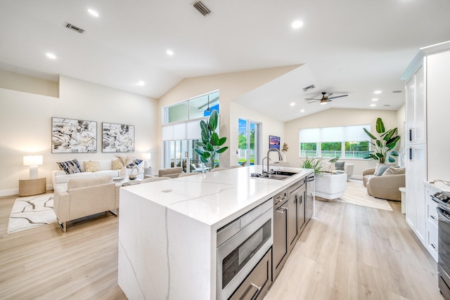 kitchen featuring ceiling fan, white cabinets, an island with sink, sink, and light wood-type flooring