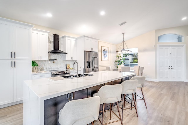 kitchen featuring a large island with sink, white cabinetry, wall chimney exhaust hood, stainless steel appliances, and sink