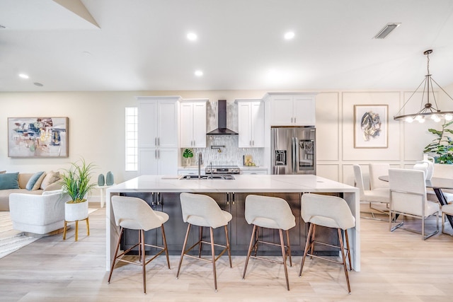 kitchen with wall chimney exhaust hood, white cabinetry, a spacious island, and stainless steel fridge with ice dispenser