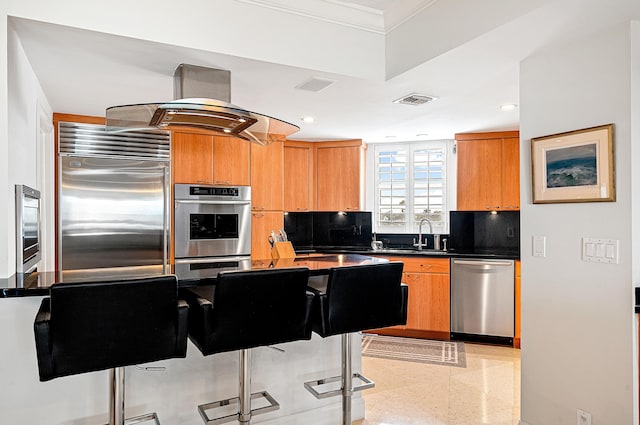 kitchen with sink, island range hood, backsplash, appliances with stainless steel finishes, and crown molding