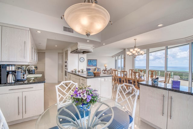 kitchen featuring dark stone countertops, pendant lighting, an inviting chandelier, and a water view