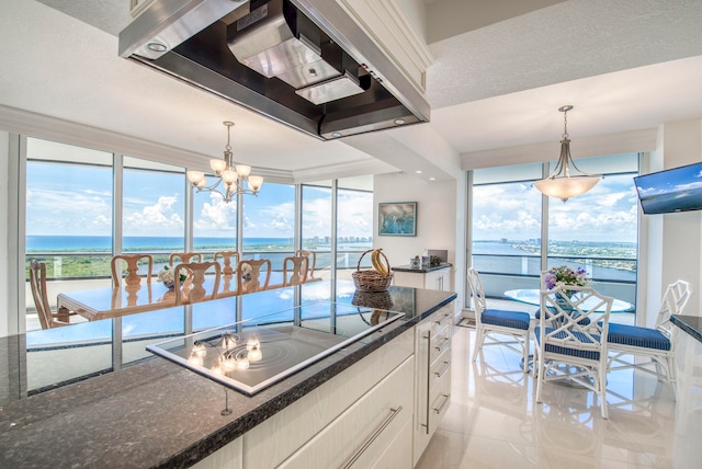 kitchen with hanging light fixtures, a water view, white cabinets, wall chimney exhaust hood, and a notable chandelier