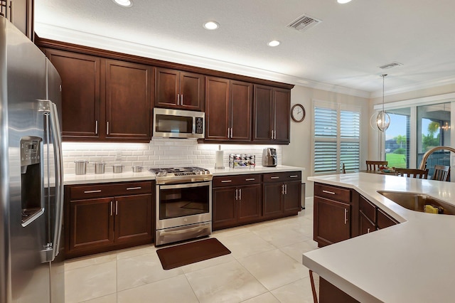 kitchen with appliances with stainless steel finishes, light tile patterned flooring, decorative light fixtures, ornamental molding, and sink