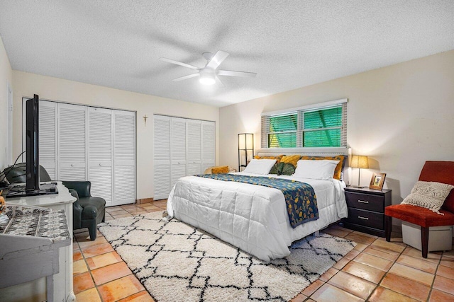 bedroom featuring a textured ceiling, ceiling fan, multiple closets, and light tile patterned flooring