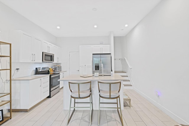 kitchen with stainless steel appliances, white cabinetry, an island with sink, a breakfast bar area, and light hardwood / wood-style flooring