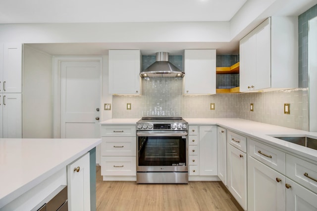 kitchen with light hardwood / wood-style flooring, wall chimney exhaust hood, stainless steel electric range oven, and white cabinetry