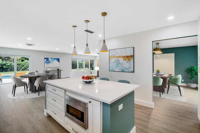 kitchen featuring stainless steel microwave, plenty of natural light, decorative light fixtures, and light wood-type flooring