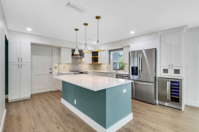 kitchen with wine cooler, a kitchen island, decorative light fixtures, wall chimney range hood, and appliances with stainless steel finishes