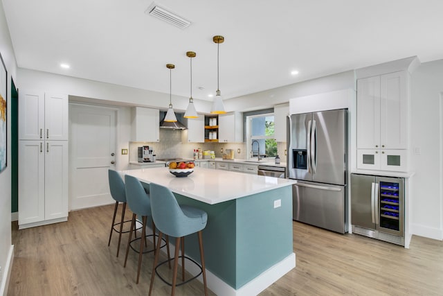 kitchen with a kitchen island, stainless steel appliances, wall chimney range hood, wine cooler, and decorative light fixtures