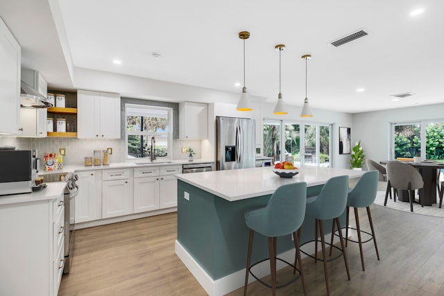 kitchen featuring white cabinets, sink, hanging light fixtures, light hardwood / wood-style flooring, and appliances with stainless steel finishes