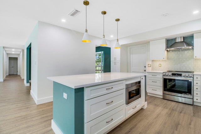 kitchen with wall chimney range hood, light hardwood / wood-style floors, hanging light fixtures, appliances with stainless steel finishes, and a center island