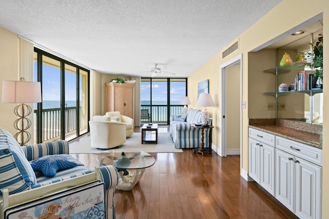 living room featuring a water view, floor to ceiling windows, dark hardwood / wood-style flooring, a textured ceiling, and ceiling fan