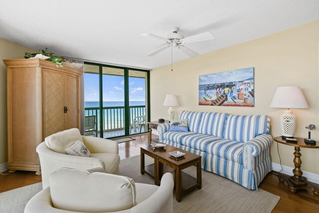 living room featuring ceiling fan, hardwood / wood-style flooring, floor to ceiling windows, and a water view