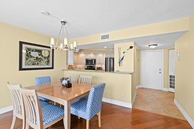 dining area with light hardwood / wood-style flooring, a textured ceiling, and an inviting chandelier