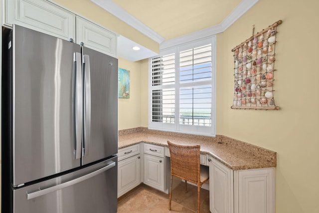 kitchen featuring built in desk, light stone counters, white cabinets, crown molding, and stainless steel fridge