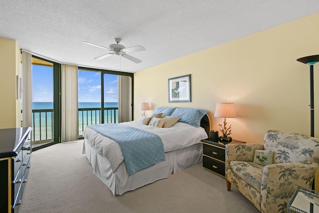 carpeted bedroom with a textured ceiling, access to exterior, a water view, ceiling fan, and expansive windows