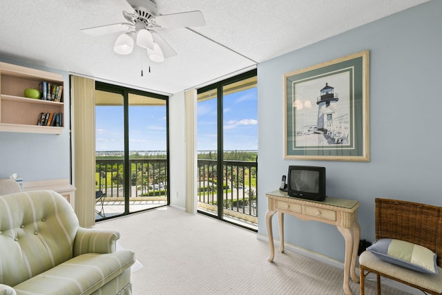 sitting room featuring a wall of windows, a textured ceiling, carpet flooring, and ceiling fan