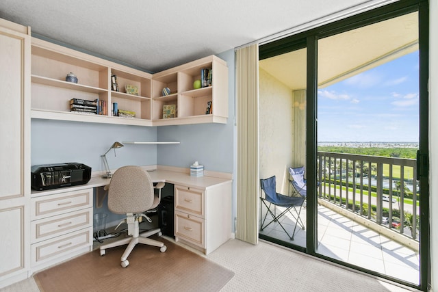 office area with a wealth of natural light, built in desk, a textured ceiling, and light colored carpet