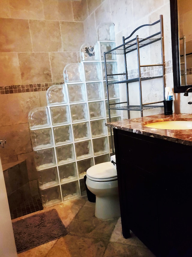 bathroom with toilet, tiled shower, vanity, and tile walls