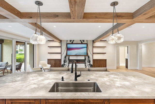 kitchen featuring light wood-type flooring, a kitchen island with sink, sink, beam ceiling, and hanging light fixtures