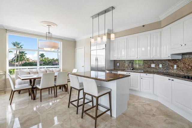 kitchen with dark stone countertops, white cabinets, built in refrigerator, and decorative light fixtures