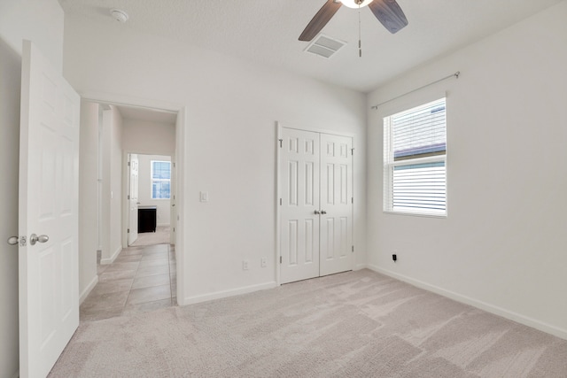 unfurnished bedroom with ceiling fan, light colored carpet, and a closet