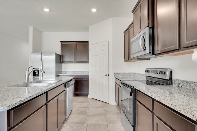 kitchen with dark brown cabinetry, light stone counters, light tile patterned floors, sink, and appliances with stainless steel finishes