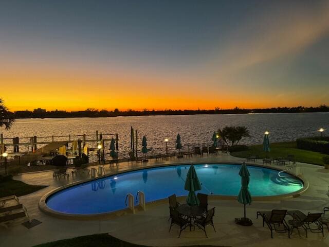 pool at dusk with a patio area and a water view