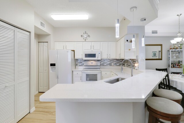 kitchen featuring hanging light fixtures, sink, white appliances, backsplash, and white cabinetry